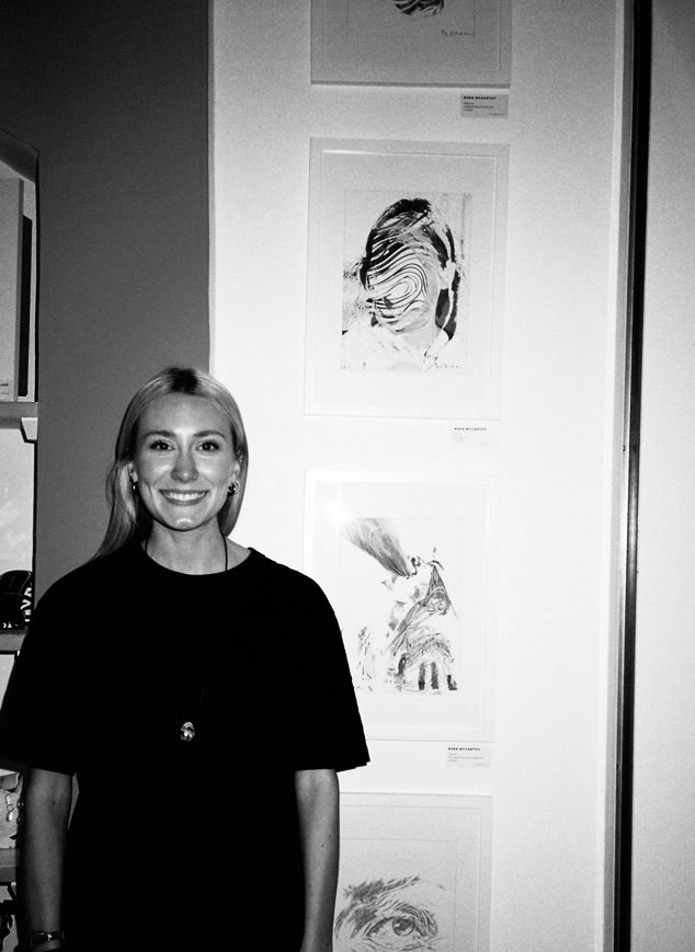 Rhea stood in front of her artwork, a black and white image with Rhea standing looking toward the camera smiling
