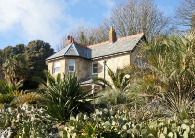 Signal Point Cottage, a yellow brick victorian lodge built within the grounds of Ventnor Botanic Garden. It's surrounded by greenery at it's vantage point within the Arid Garden.